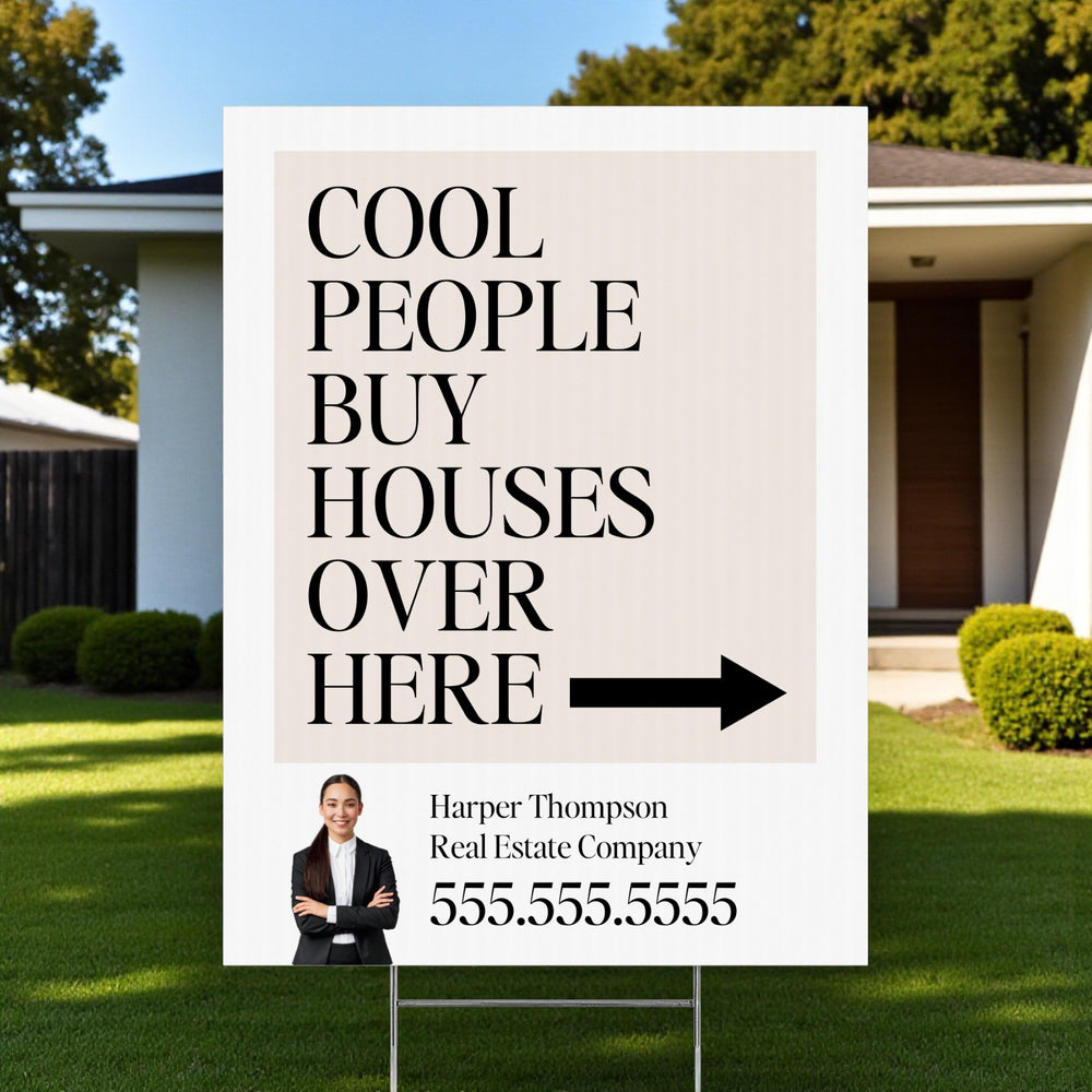 Real estate sign with text 'Cool people buy houses over here' in front of a house.